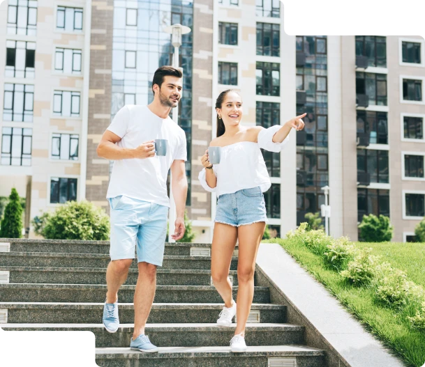 Para w letnich ubraniach na tle apartamentowców, wskazująca na coś w oddali.